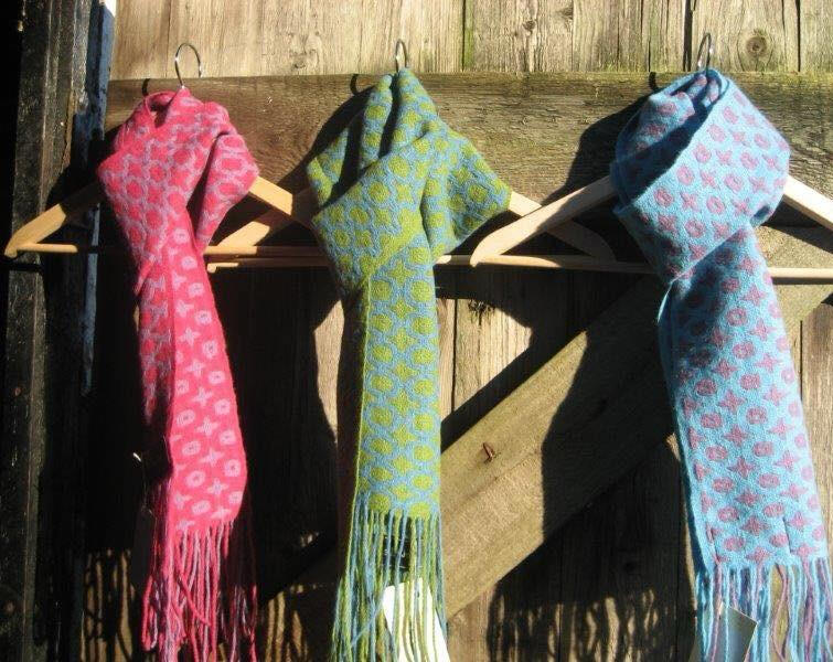 Trio of handwoven scarves in pink, green, and blue displayed vertically