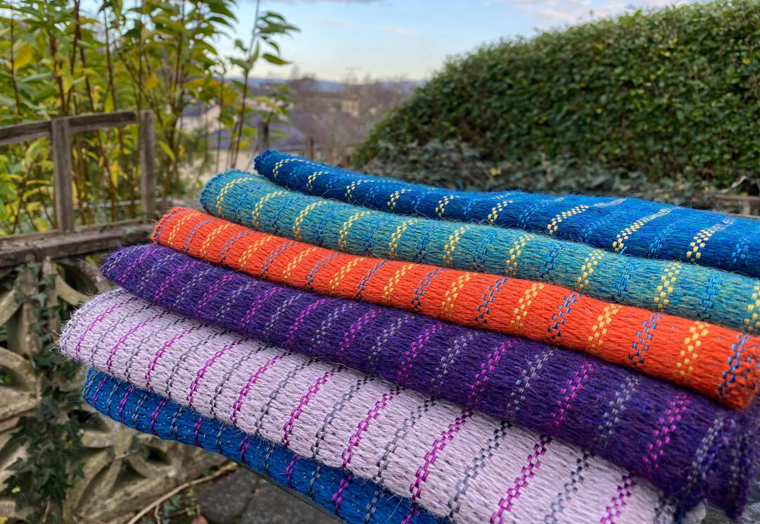 Stack of six folded handwoven scarves with countryside views in Cumbria
